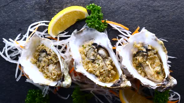 Fresh Raw Oysters in Shells with Lemon and Fried Garlic on Black Textured Slate alt