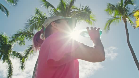 Woman Drinks Water Relaxing Outdoors in Tropical Park in Summer Sunny Day alt