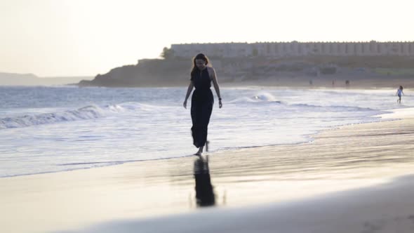 Young Woman in Long Evening Dress Walking Along Atlantic Ocean Beach at Sunset