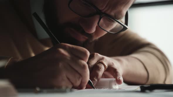 Concentrated Man with Beard Glasses Works with Drawings Makes Notes alt