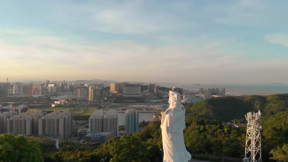 Rotating aerial view of Goddess A-Ma looking over Macau cityscape during sunset alt