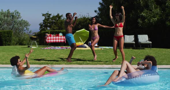 Diverse group of friends having fun dancing playing on inflatables in swimming pool alt