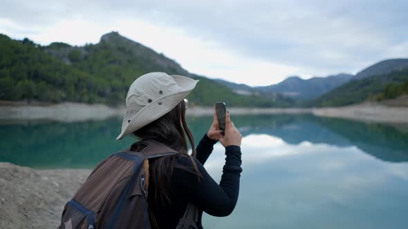 Young Woman in Hat Films Lake and Mountains in Spain with Phone Slomo alt