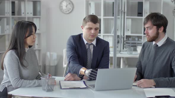 Businessman with Prosthetic Hand Speaking with Colleagues at Office Meeting alt