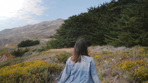 Camera Follows Young Happy Woman Running Along a Small Path Towards Big Rocks and Forest at Big Sur alt