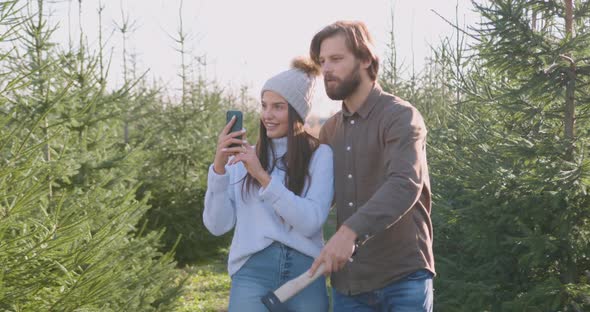 Man with Ax Offering Different Versions of fir Trees to His Pretty Joyful wife alt