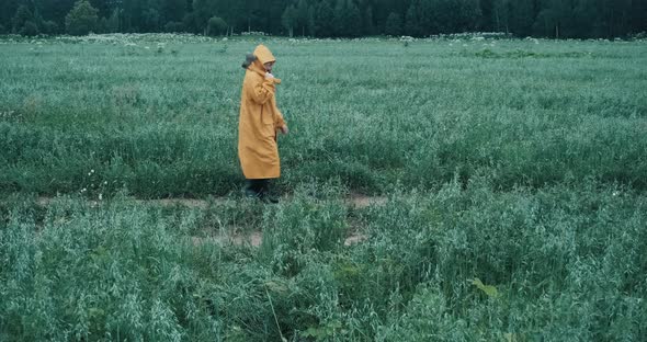 Man in Yellow Raincoat and Carrying an Axe is Walking Through Field at Dusk