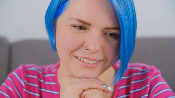 Video portrait of beautiful girl with colored blue hair looking in laptop with cheerful smile alt