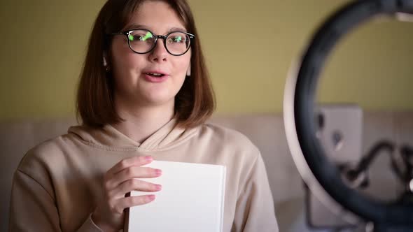 Girl book blogger with eye glasses recording vlog on digital smartphone cam alt