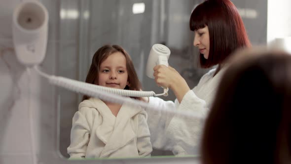 Mother is Brushing and Drying Child Hair After Shower Standing in Front of a Mirror in the Bathroom alt