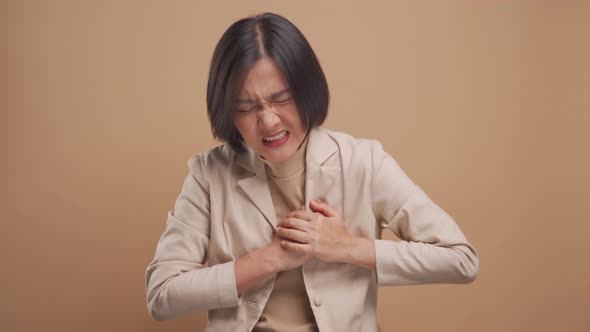 Asian business woman was sick with chest pain and standing isolated over beige background. 4K video