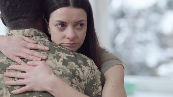 Closeup Portrait of Sad Young Caucasian Woman Hugging African American Man in Camouflage Uniform alt