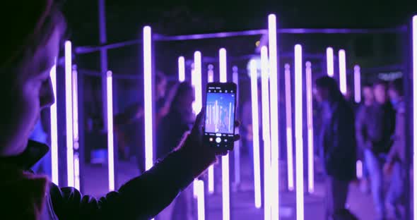 Young Female Recording Video of Neon Lights Performance Show at Night with Smartphone alt
