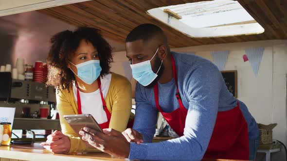 African american couple wearing face masks using digital tablet in the food truck alt