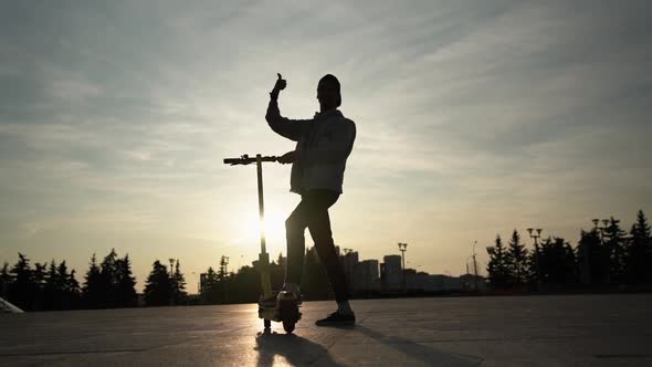 Long Shot: Silhouette of Man with Scooter, Who Shows Thumbs Up, 4x Slowmotion alt