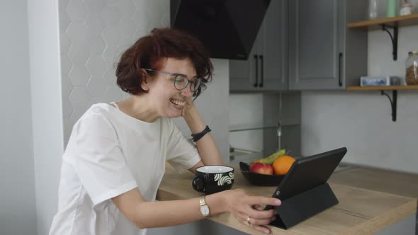 Smiling Young Woman Sitting in Kitchen Drinking Tea and Talking Video Call Having Online Conference