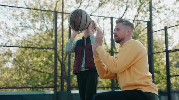 Father Explaining to Son How to Hold and Throw a Basketball Ball on a Sunny Day