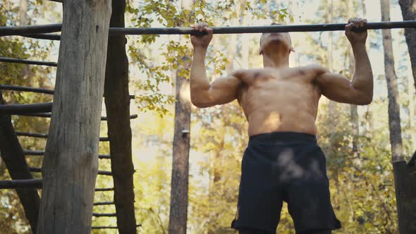 Man is doing pull ups exercises on horizontal bar in the forest gym, outdoors