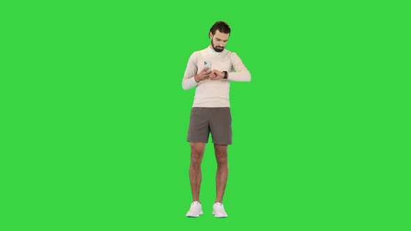 Fitness Man with Mobile Phone Connected to a Smart Watch on a Green Screen Chroma Key alt