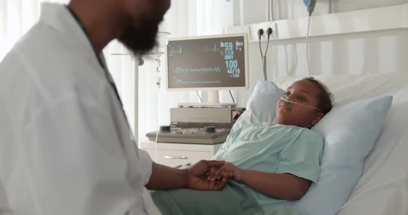 African Child Lying in Bed in Hospital Room with Doctor Comforting Her and Holding Hand alt