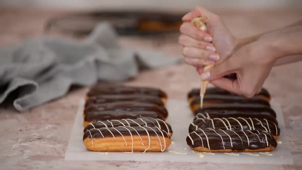 Pastry chef pours white chocolate on French eclairs.