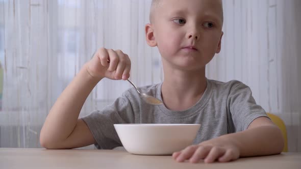 Satisfied little boy eating cereal with milk for breakfast. alt