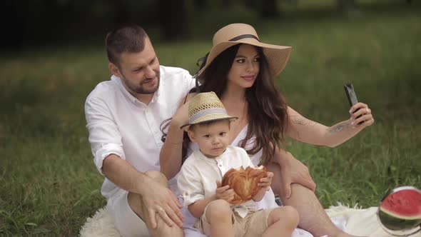 Beautiful Husband and Cute Wife Take Selfies in the Park Whith Their Little Child