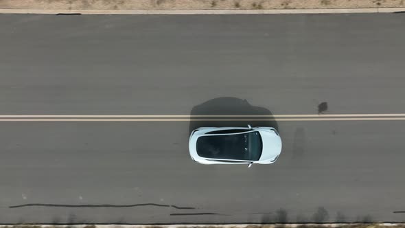 Top down aerial of glass rooftop of Tesla Model 3 driving on open road. Aerial tracking shot. alt
