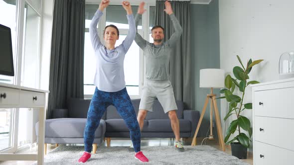 Caucasian Couple is Doing Jumping Jacks Exercise at Home in Cozy Bright Room Slow Motion alt