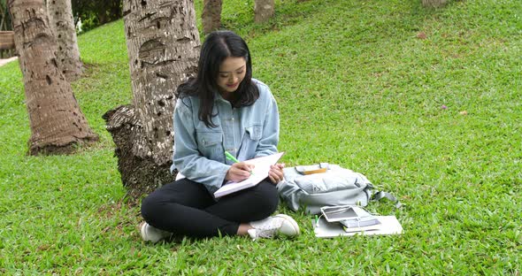 Asian Girl Student Writing Something On Notebook In The Park alt