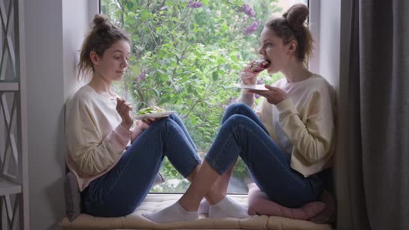 Slim Beautiful Identical Twins Eating Healthful Salad and Unhealthy Sweet Bun alt