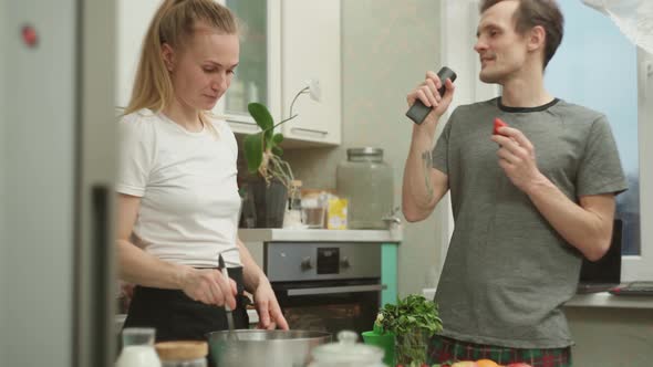 Joyful Guy Singing and Dancing Near Girlfriend Cooking in Kitchen