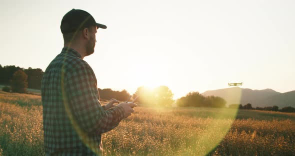 Tracking shot of drone ascending into blue sky during sunset. Young man with cap flying alt