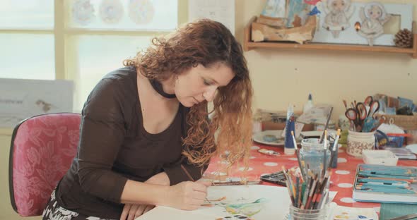 Female artist painting in her studio with water colors and pencils alt