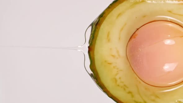 Slow Motion of Flowing the Juice and Oil Stream From Avocado Slice on White Background alt