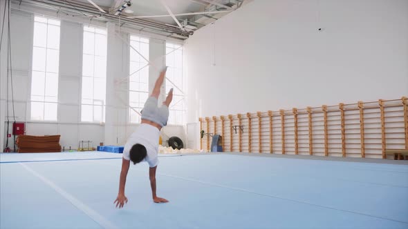 A Teenager Boy is Doing a Cartwheel and a Triple Back Flip in Gym Steadicam alt