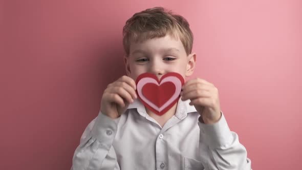 Caucasian Boy Holds Heart Shaped Valentine on Pink Background
