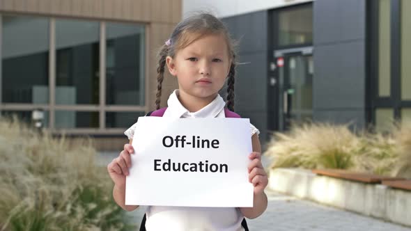 Serious Little Schoolgirl with Pigtails Stands with OFFLINE EDUCATION Poster Outside the School alt