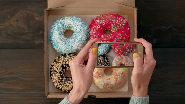 Woman's Hands Take Pictures with Smartphone of Delicious Donuts in Box alt