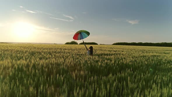 Girl with Multicolored Umbrella Walking in Field alt