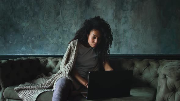 Young Attractive AfricanAmerican Woman Using Laptop Computer Sitting on Sofa at Home alt