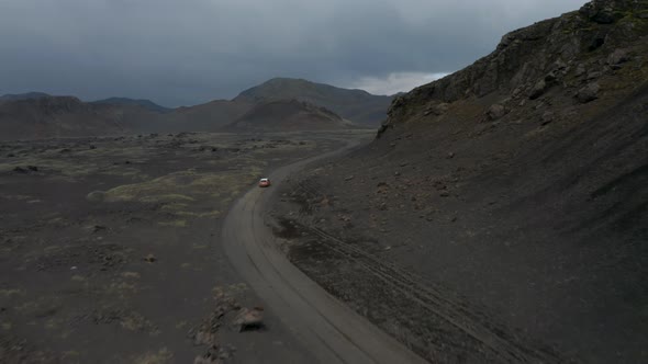 Aerial View of Fast Moving Car Driving on Dirt Road Around Mountain Ridge alt
