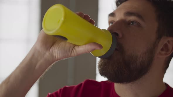 Bearded Man Drinking Water While Resting After Home Exercise Routine alt