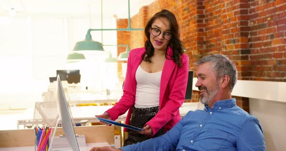Male and female executives discussing over digital tablet at desk alt