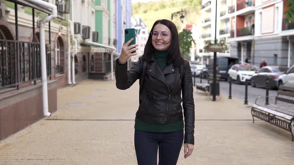 Happy young girl making a video call, smiling, talking on the background of a city street. alt