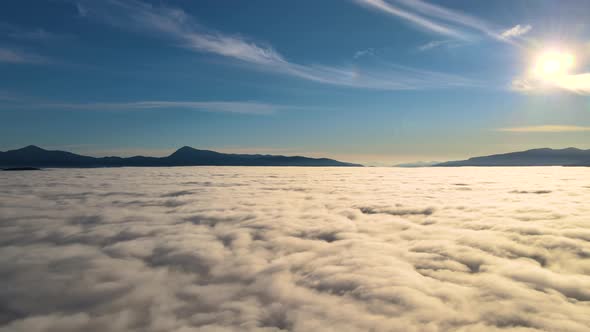 Aerial view of vibrant sunset over white dense clouds with distant dark mountains on horizon. alt
