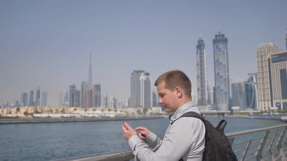 The Man Dials the Number on the Phone and Talks on the Background of the Panorama of Dubai alt