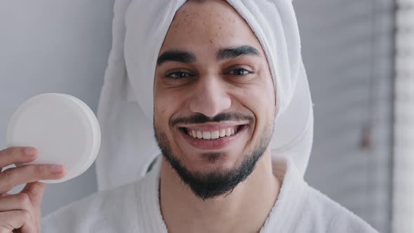 Arabian Hispanic Indian Man with Towel on Head Holding Jar of Cream for Face Laugh Looking at Camera alt