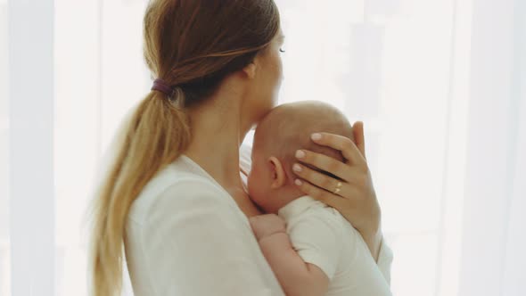 Back View of the Caucasian Mother Holding and Swings Her Newborn Baby Before Sleeping and Kissing alt