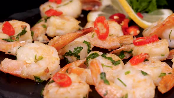 Cooked and grilled shrimps with lemon slice, chilli pepper and parsley rotating on a black plate